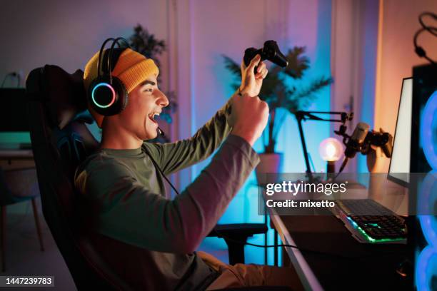 young teenager plays the computer and celebrates victory in video game with a clenched fist and a smile - spel bildbanksfoton och bilder