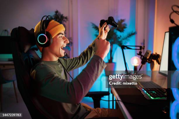 young teenager plays the computer and celebrates victory in video game with a clenched fist and a smile - videospel bildbanksfoton och bilder