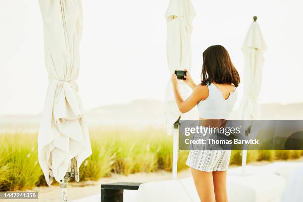 medium wide shot of teenage girl taking photo of sunset at beach resort - one teenage girl only bildbanksfoton och bilder