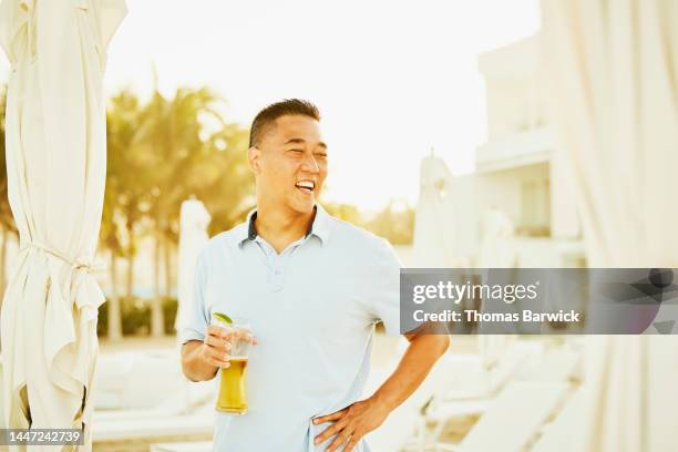 medium shot of laughing man relaxing on beach at tropical resort - true luxury stock-fotos und bilder