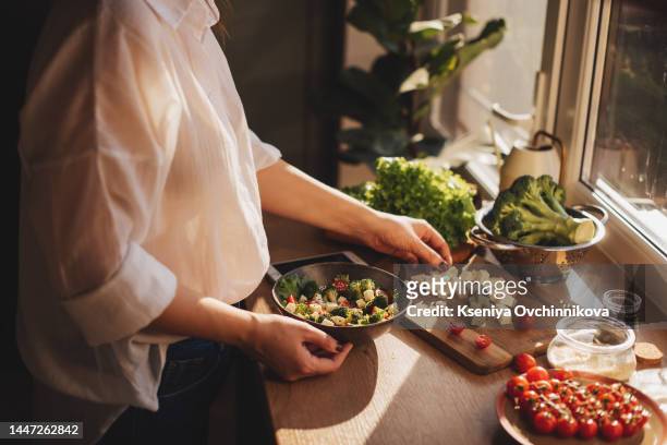 healthy dinner or lunch. woman in t-shirt and jeans standing and holding vegan superbowl or buddha bowl with hummus, vegetable, salad, beans, couscous and avocado and smoothie in hands, square crop - buddha hands stock-fotos und bilder