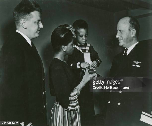 Mrs. Charles W. David, Jr.; African American widow and her three-year-old son, Neil Adrian receiving the Navy and Marine Corps Medal from Rear...
