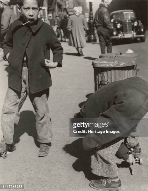 105th Street - Two boys playing with roller skates, each wearing a single roller skate on their right foot, East Harlem, New York City, 1947 Creator:...