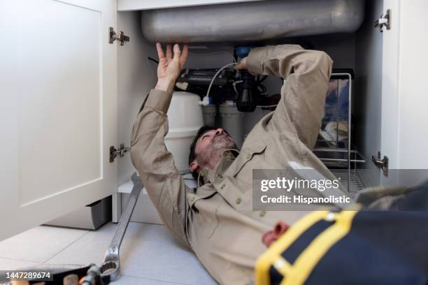 plumber fixing a leak on a pipe in the kitchen - handyman stockfoto's en -beelden