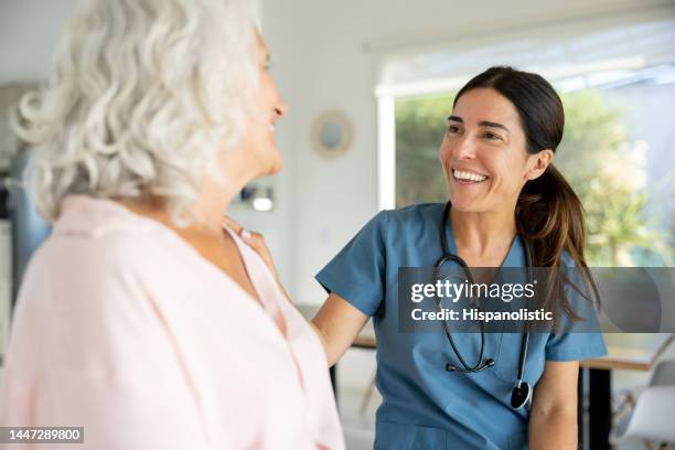 glücklicher arzt spricht mit einer älteren frau bei einem hausbesuch - adult patient with doctor and stethoscope stock-fotos und bilder