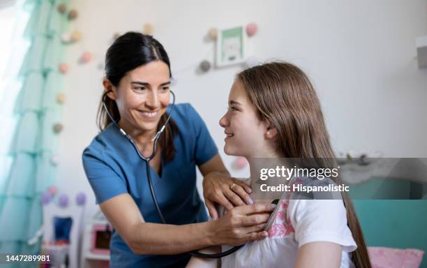 happy doctor performing a medical exam on a girl during a house call - auscultation woman stockfoto's en -beelden