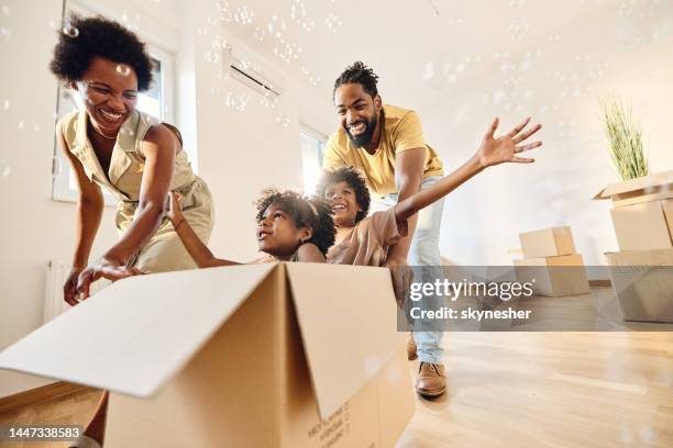 unbeschwerte schwarze familie, die spaß hat, nachdem sie in ein neues zuhause gezogen ist. - man boxes moving home stock-fotos und bilder