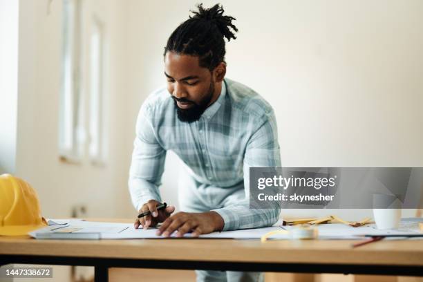 smiling black architect examining plans in the apartment. - interior design professional stock pictures, royalty-free photos & images