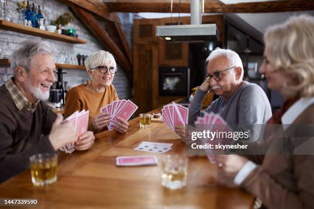glückliche ältere freunde genießen es, zu hause karten zu spielen. - kartenspiel tisch stock-fotos und bilder