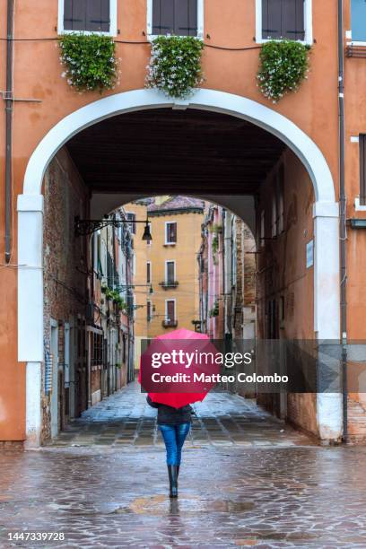 woman with red umbrella walking in a small alley - castello stockfoto's en -beelden