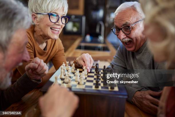 happy senior friends playing chess at home. - senior playing chess stock pictures, royalty-free photos & images