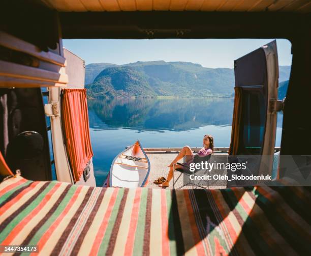 mujer descansando cerca de la autocaravana cerca del lago en noruega - luxury camp fotografías e imágenes de stock