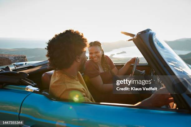 woman driving by boyfriend sitting in car - auto convertibile photos et images de collection