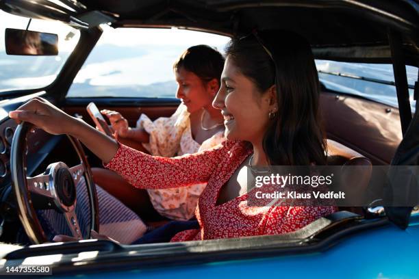 woman driving car by friend using smart phone - floral pattern dress stock-fotos und bilder