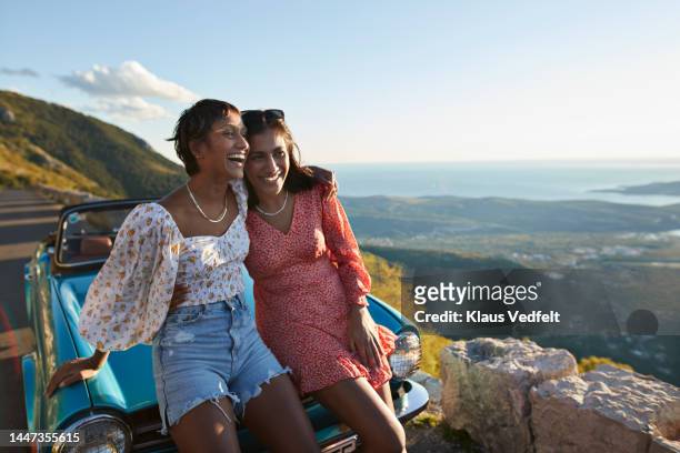 woman with arm around female friend leaning on car - travel fotografías e imágenes de stock