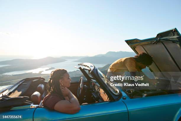 woman looking at boyfriend examining car breakdown - carro quebrado - fotografias e filmes do acervo