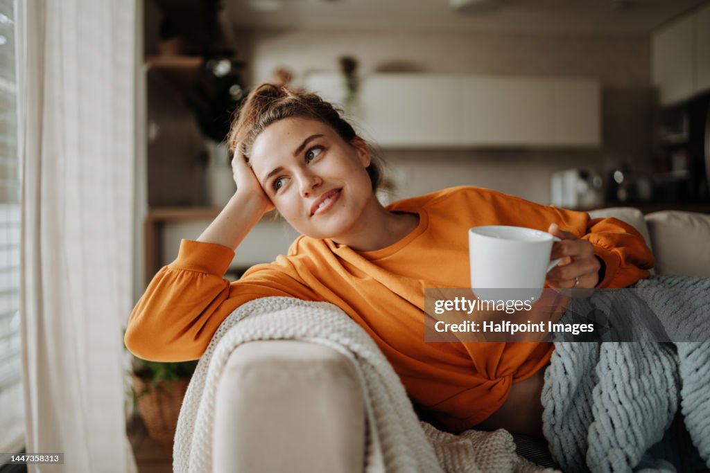 Young woman resting on sofa with cup of tea.