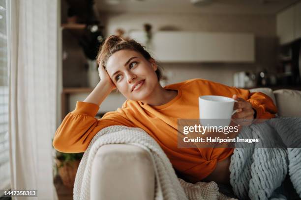 young woman resting on sofa with cup of tea. - contento fotografías e imágenes de stock