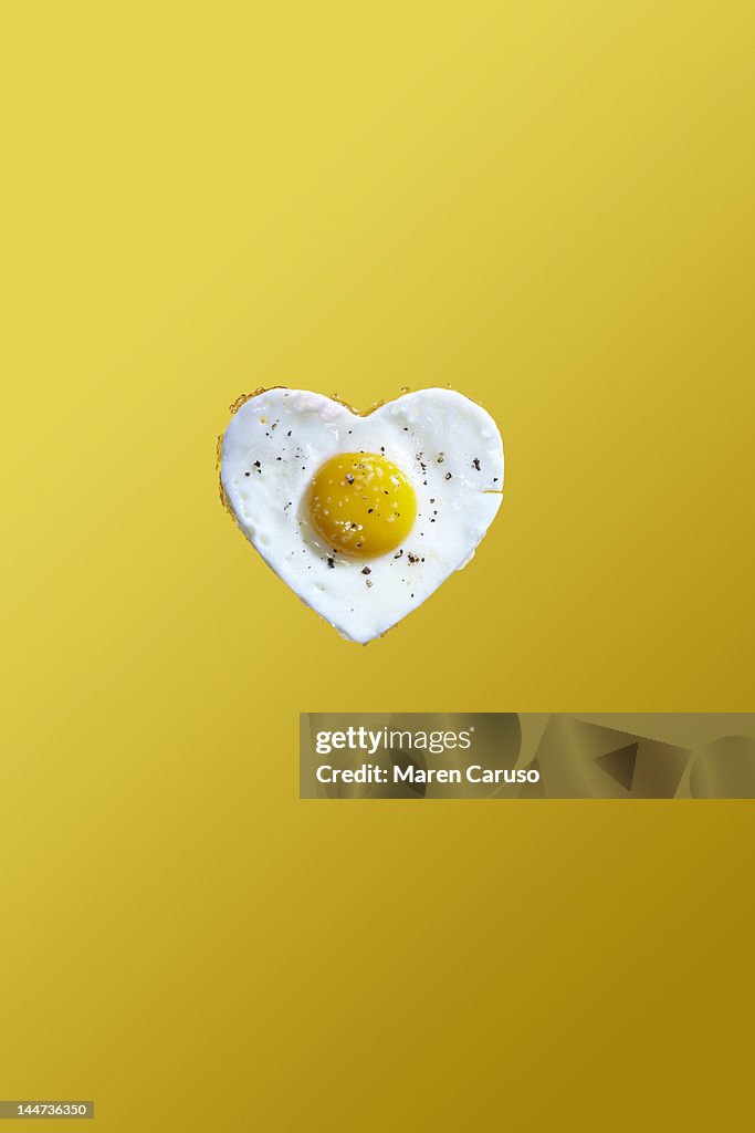 Heart shaped fried egg on yellow background