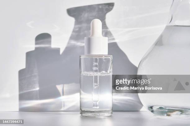 a transparent bottle with serum and a container with water on a white background in the rays of the sun with shadows. - 容器 ストックフォトと画像