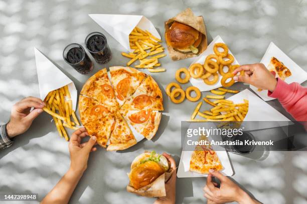 human hands with assorted take out food such as pizza, french fries, onion rings, burger and cola. - ready meal fotografías e imágenes de stock