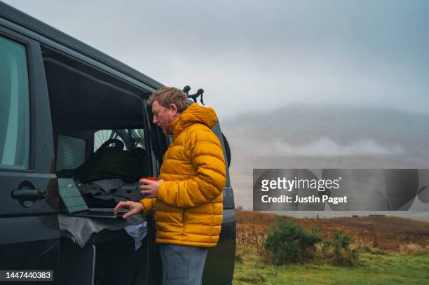 mature man catches up with some work whilst in his campervan in the scottish highlands - labor camp fotografías e imágenes de stock