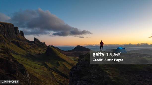 drone view of a man taking in the beautiful sunrise view over the quiraing - tent stock pictures, royalty-free photos & images