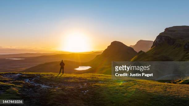 drone view of a man in red puffer coat taking in a beautiful sunrise view in the quiraing on the isle of skye. he's accompanied by his pet chocolate labrador dog - quiraing stock pictures, royalty-free photos & images
