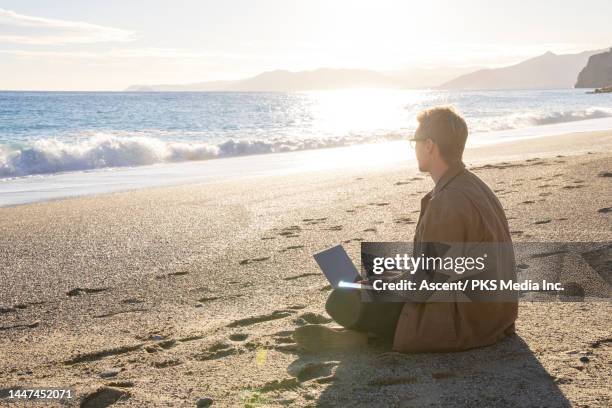 young man uses laptop on beach at sunset in autumn - profileren stockfoto's en -beelden