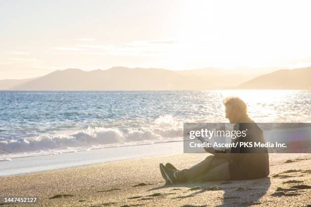 man uses digital reader on beach at sunset in autumn - produced segment stock pictures, royalty-free photos & images