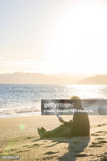 man uses digital reader on beach at sunset in autumn - imagem em movimento - fotografias e filmes do acervo