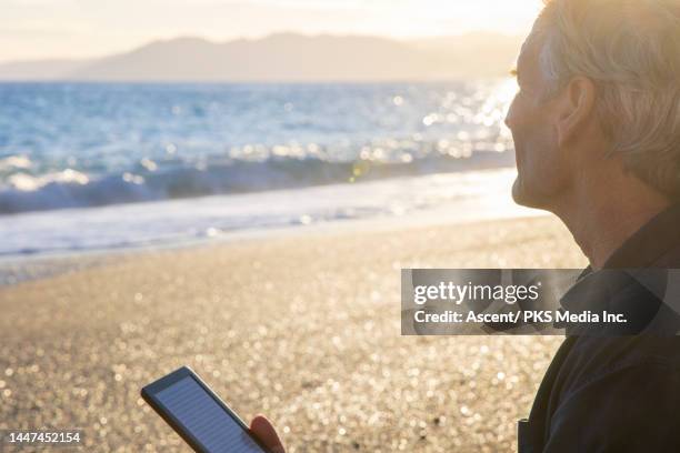 man uses digital reader on beach at sunset in autumn - produced segment stock pictures, royalty-free photos & images