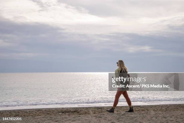 senior woman walks on beach with phone - moving image stock pictures, royalty-free photos & images