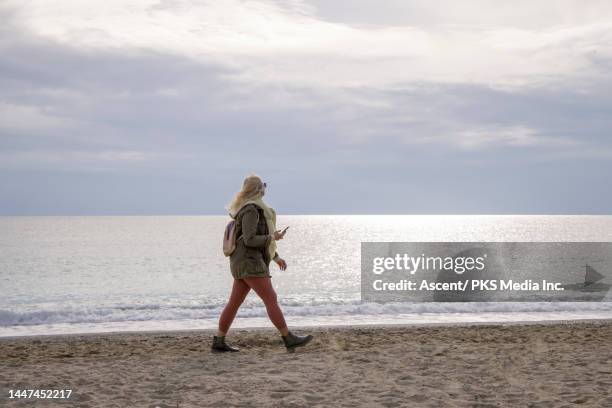 senior woman walks on beach with phone - woman profile stock pictures, royalty-free photos & images