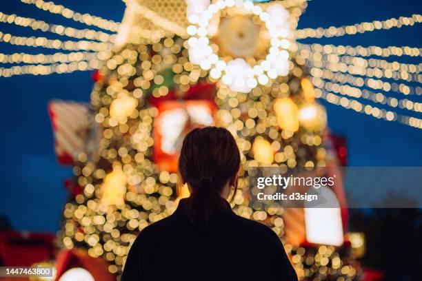 rear view of young asian woman looking at an illuminated christmas tree with decorated christmas lights in the city. enjoying christmas atmosphere. holiday and festive vibes. christmas is almost here - christmas celebrations in china imagens e fotografias de stock