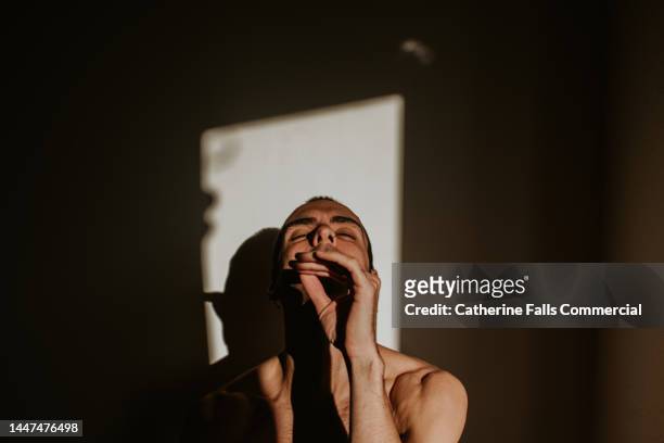 conceptual, simple image of a topless man, partially illuminated, mid-pose during a performance - muse band stock pictures, royalty-free photos & images
