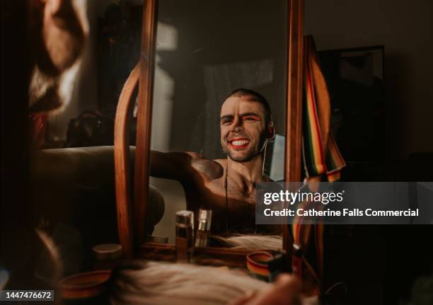 a smiling, confident gay man smiles as he looks at his reflection in a vanity mirror - beautiful transvestite - fotografias e filmes do acervo