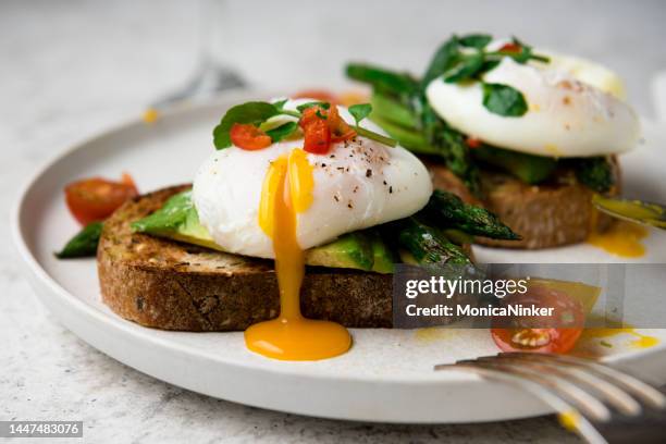 uova in camicia su pane tostato con avocado, asparagi, pomodori e germogli per una sana colazione - tuorlo foto e immagini stock