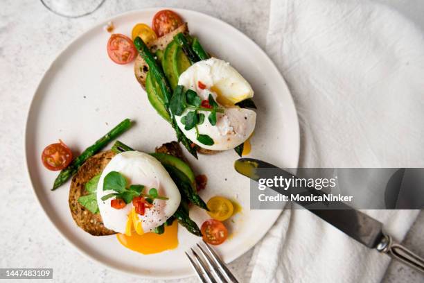 huevos escalfados en tostadas con aguacate, espárragos, tomates y brotes para un desayuno saludable - escalfado fotografías e imágenes de stock