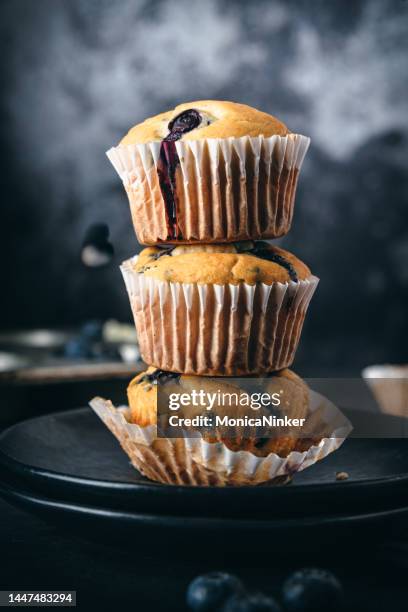 stack of homemade blueberry muffins in paper cake cases surrounded by fresh blueberries. - forma de queque imagens e fotografias de stock