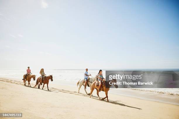 Wide shot of family on horseback ride on tropical beach during vacation