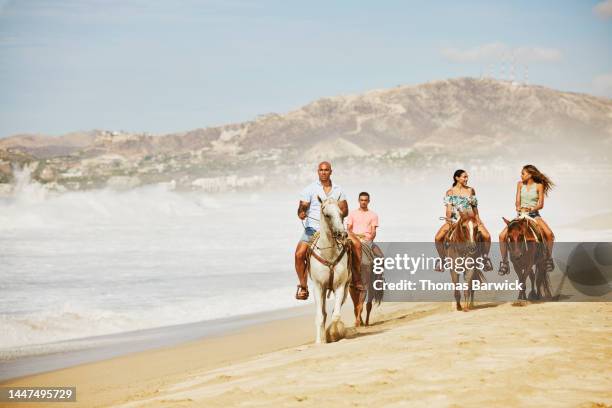 wide shot of family on horseback ride on tropical beach during vacation - horse front view stock pictures, royalty-free photos & images