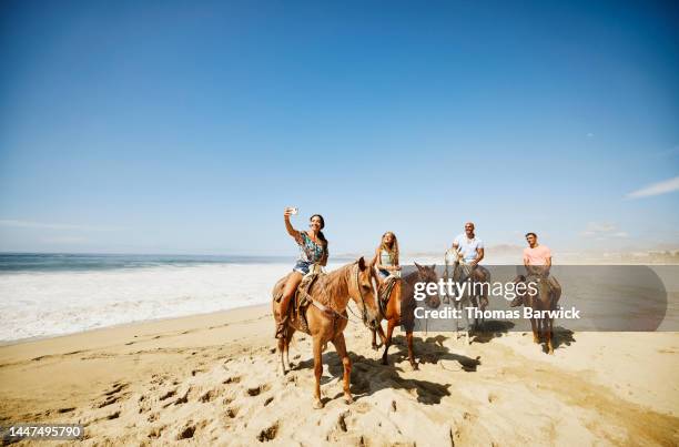 wide shot of mother taking selfie with family while riding horses on beach - animal selfies 個照片及圖片檔