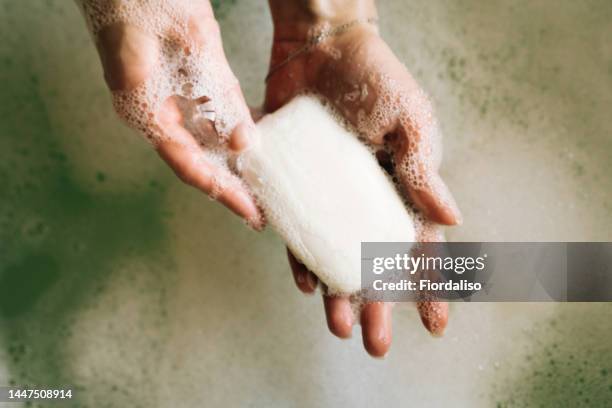 white toilet soap in female hands against the background of a fragrant foam bath. natural beauty, daily skincare routine. moisturizing, cleansing - soap stock-fotos und bilder