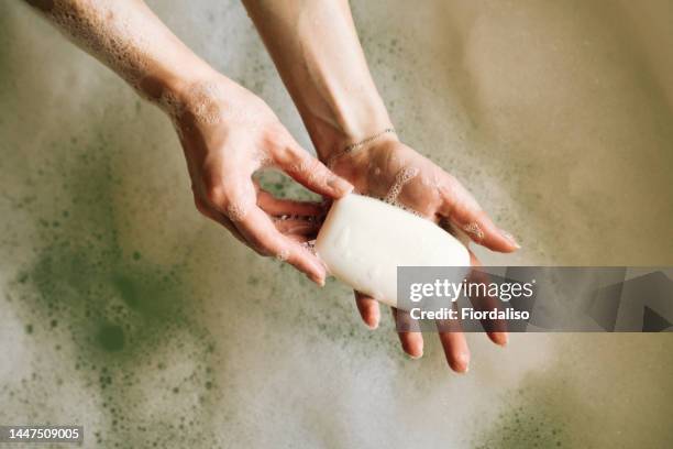 white toilet soap in female hands against the background of a fragrant foam bath. natural beauty, daily skincare routine. moisturizing, cleansing - woman bath bubbles stock pictures, royalty-free photos & images