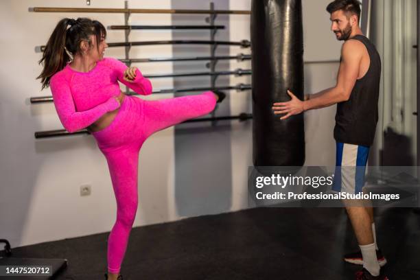 a young sportswoman is punching a bag in a gym while a coach is assisting her. - martial arts instructor stock pictures, royalty-free photos & images