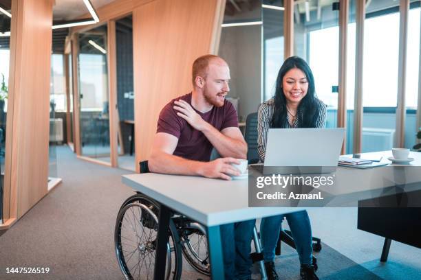 young caucasian man in a wheelchair using laptop with hispanic woman intern - disability computer stock pictures, royalty-free photos & images