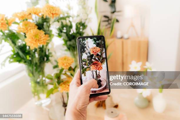 close-up of hand holding a mobile phone and taking photos to a bouquet of yellow flowers - hacer foto fotografías e imágenes de stock