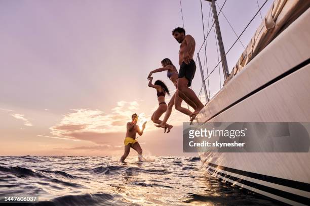 below view of carefree people jumping into sea from boat at sunset. - istria stock pictures, royalty-free photos & images