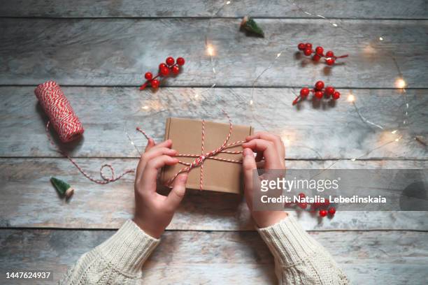 hands close-up packing christmas gift in brown box. top view, wooden background - gift lounge stock-fotos und bilder